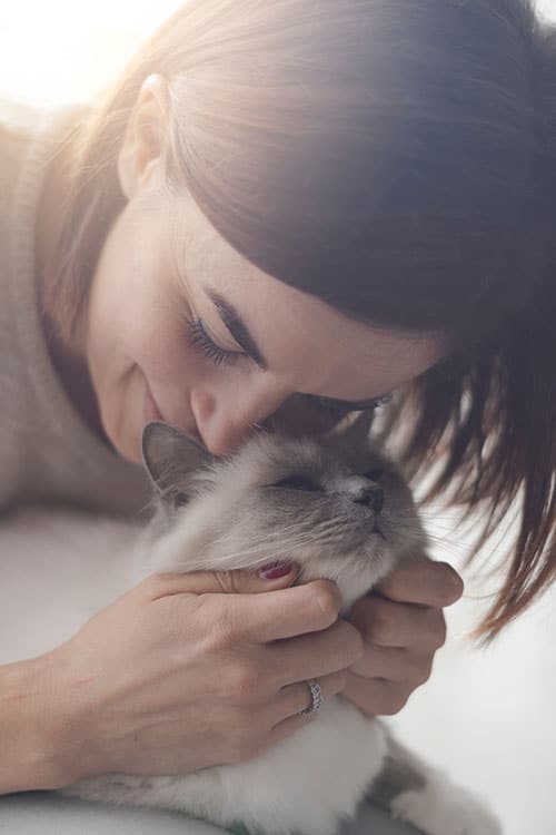 A woman, reminiscent of a caring veterinarian, lovingly cradles a fluffy cat, pressing her forehead against its head. The scene is softly lit, creating a warm and tender atmosphere.